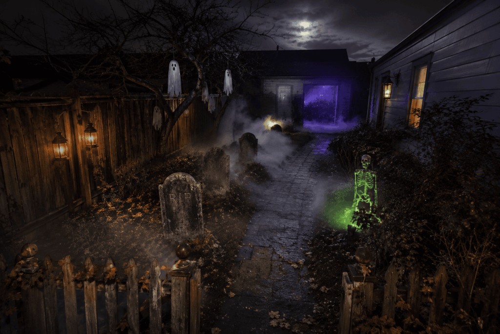 Vue d'un jardin transformé en parcours hanté pour Halloween avec cimetière, brume basse et garage illuminé au fond