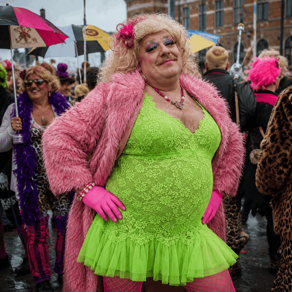 Homme carnavaleux d’une cinquantaine d’années portant une robe vert fluo, un manteau en fausse fourrure rose, une perruque blonde, du maquillage festif et des collants résille, dans une foule joyeuse avec parapluies colorés au Carnaval de Dunkerque.