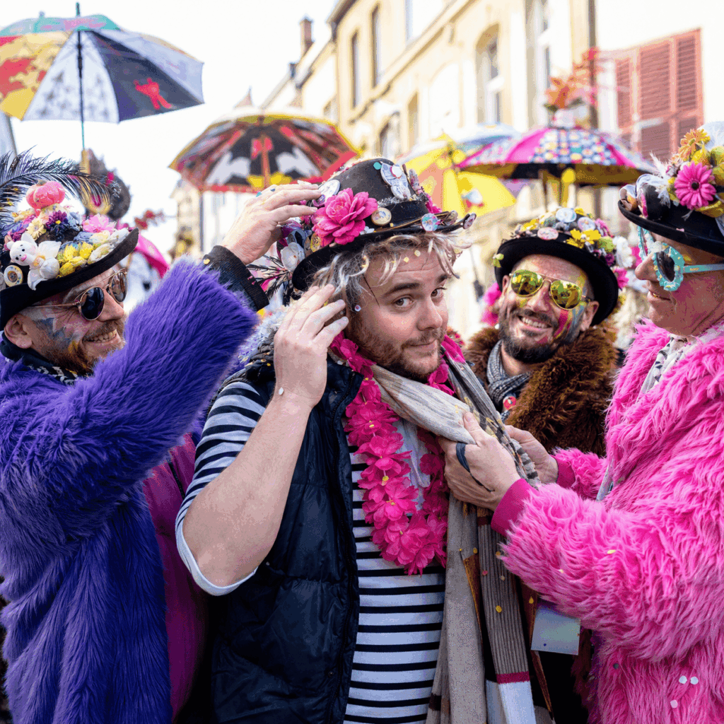 Carnavaleux débutant dans une rue festive d’hiver, avec tenue trop légère, perruque de travers et chapeau mal fixé, aidé par des amis mieux préparés portant manteaux en fausse fourrure colorés, chapeaux décorés, lunettes fantaisie et accessoires de clet’che pour le Carnaval de Dunkerque.
