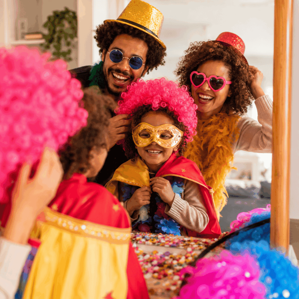 Famille souriante essayant des accessoires de Carnaval devant un miroir avec perruques, chapeaux, lunettes et masques.